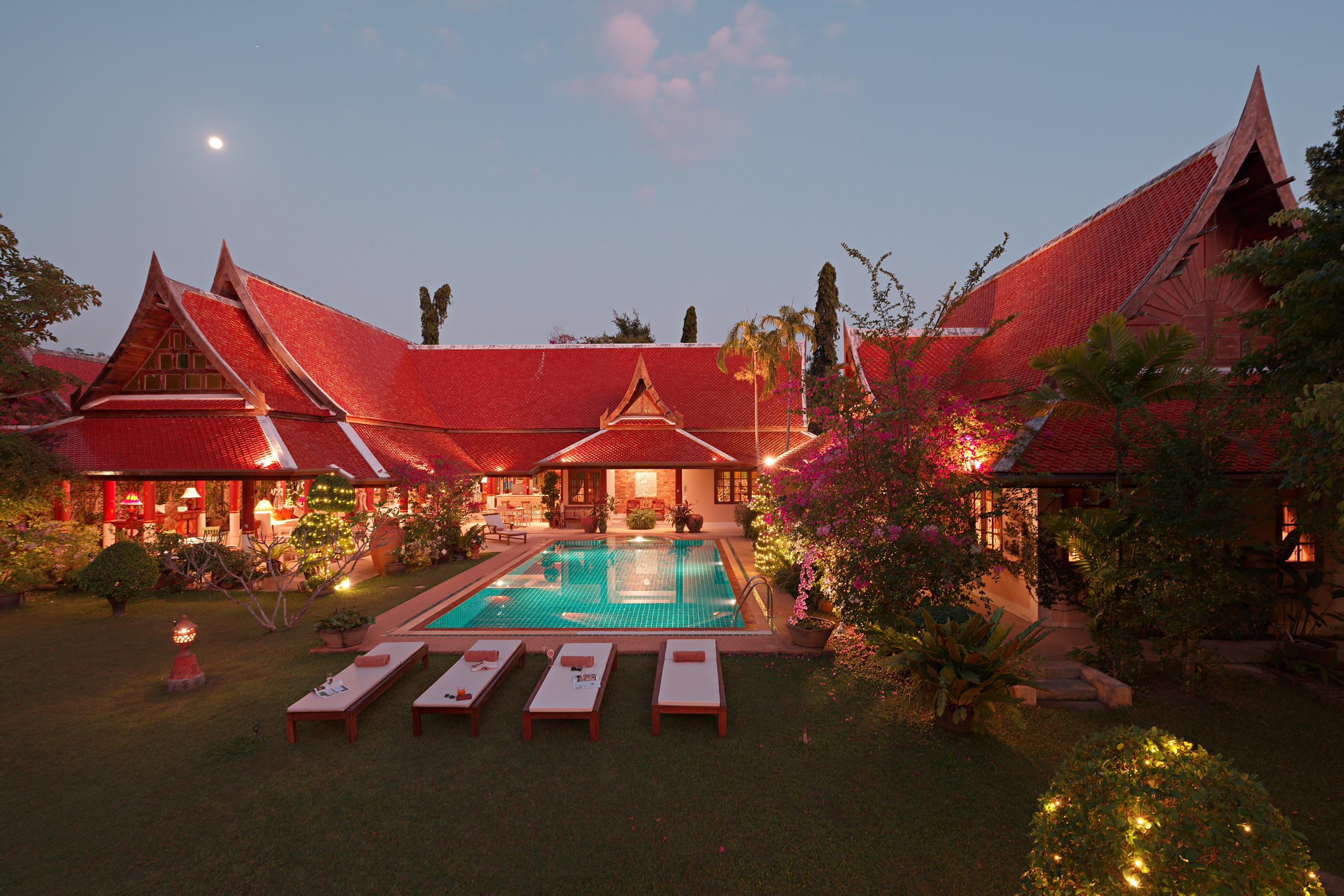 Villa Semaya at dusk, pool and lawn lit under the Thai roofs